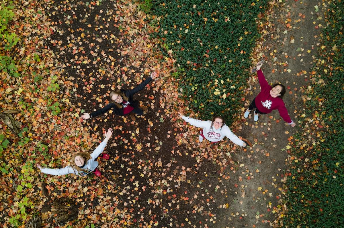 俯拍的三个学生在秋天的一条枝繁叶茂的小路上伸开双臂，对着镜头微笑